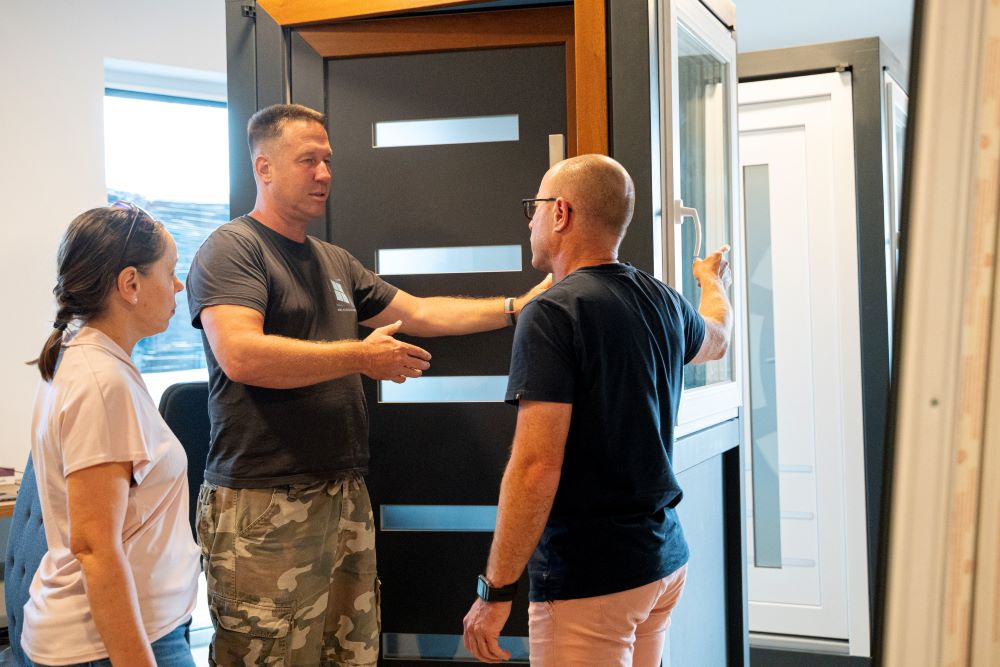 Ablakdiszkont munkatársa bemutatja a nyílászárókat a bemutatóteremben két vevőnek